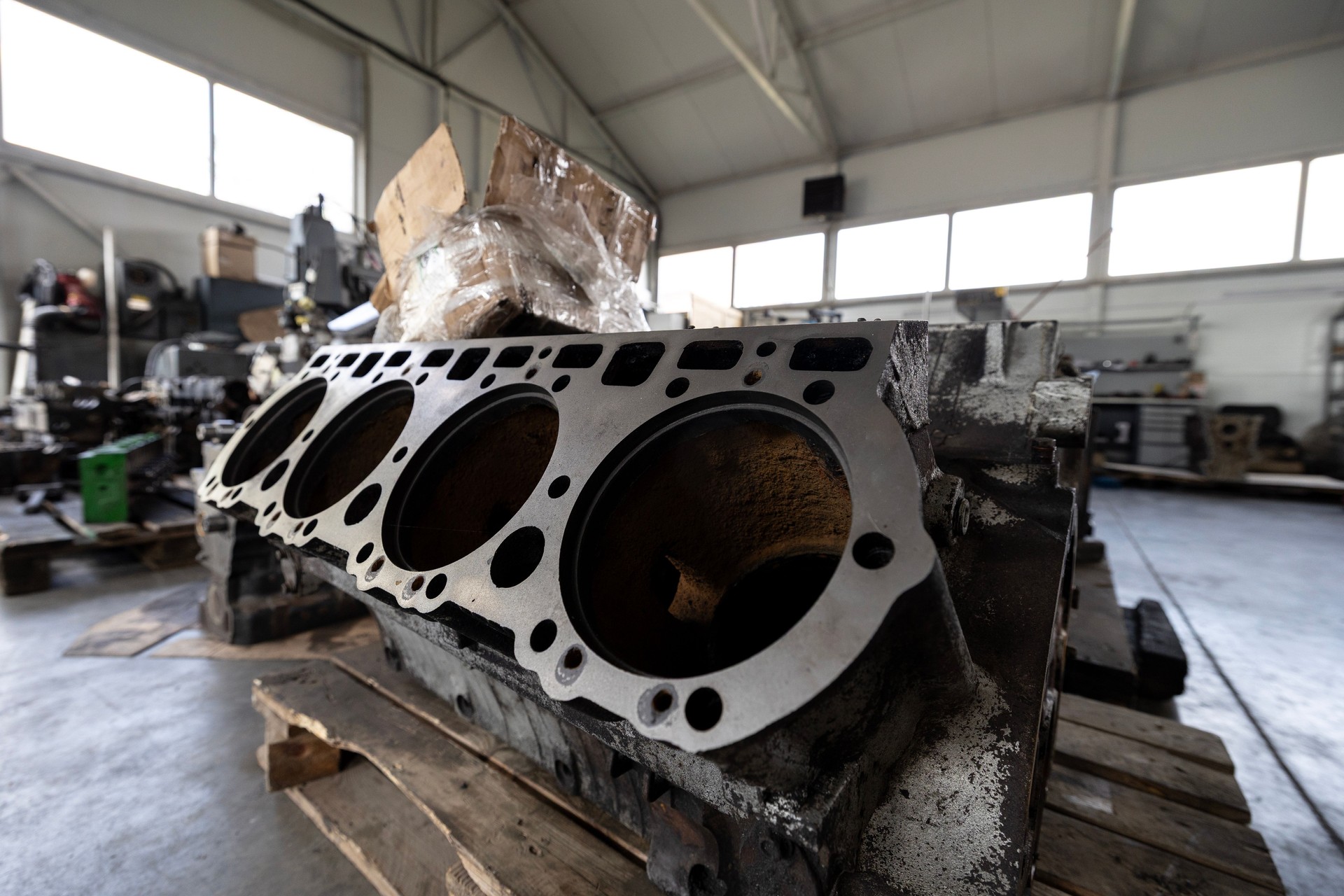 A engine block rests on wooden supports in a repair shop or warehouse, prepared for maintenance or rebuilding.